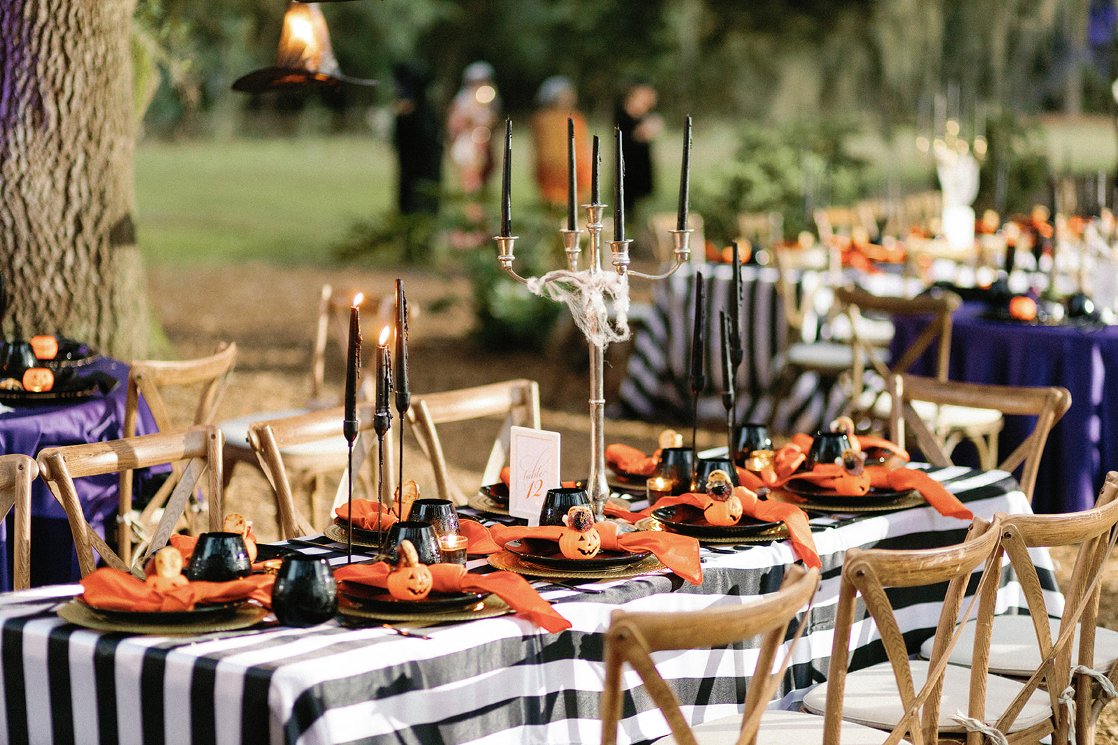 Table set for a Halloween party with a black and white striped tablecloth, orange accents and a small pumpkin at every place setting