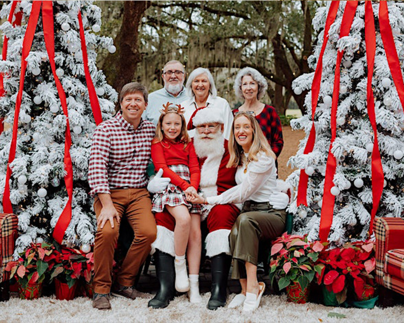 Happy family posing for a photo with Santa surrounded by Christmas trees and poinsettias