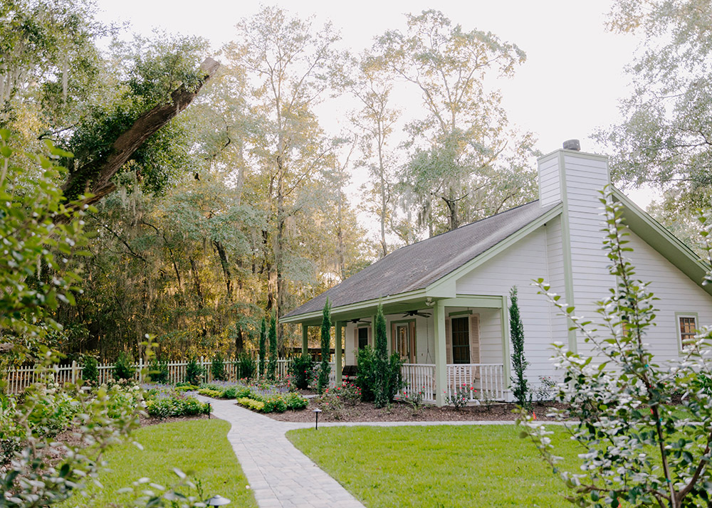 white cottage with green trim surrounded by a charming garden