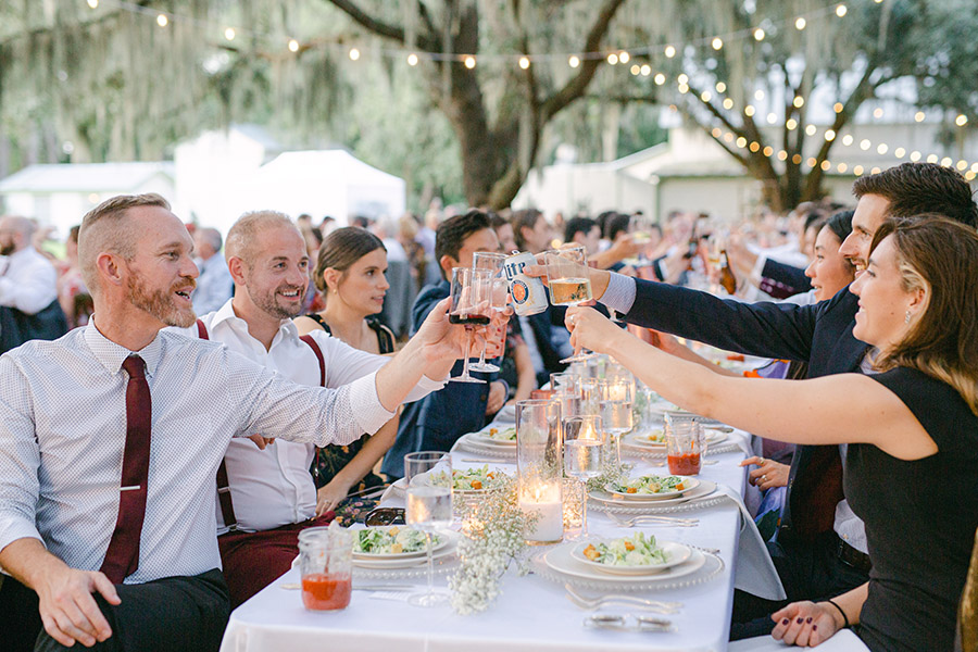 Guests clinking glasses at a candlelit table under live oak trees