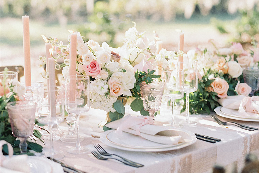 An elegant table setting surrounded by taper candles and flower arrangements in blush and white
