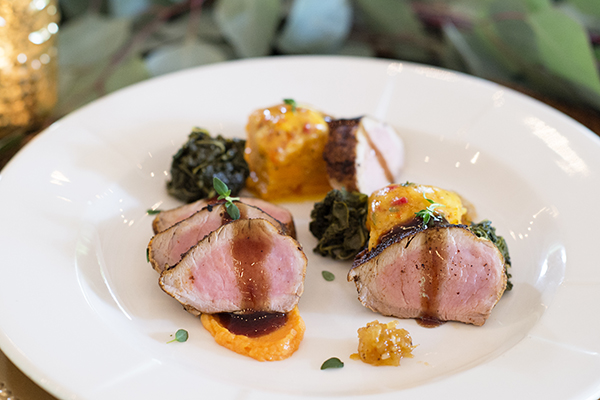 artfully plated dinner of pork tenderloin cooked to perfection with colorful vegetables, sauce, and garnish