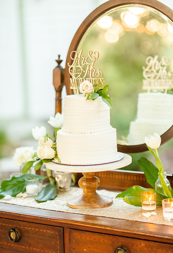 Two-tier wedding cake on a wooden cake stand sitting on a vintage wash stand with mirror