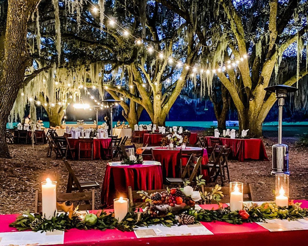tables set under a canopy of live oaks and lit by glowing cafe lights and candles