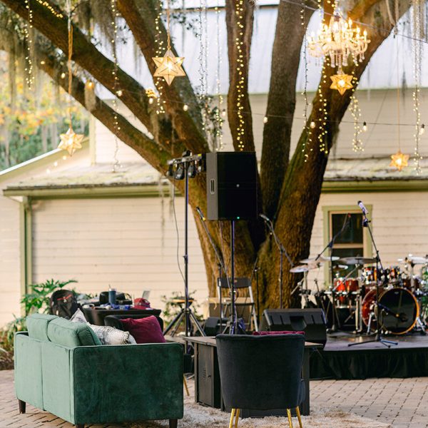 A stage adorned with a variety of band instruments beneath an oak tree, featuring a chandelier hanging above.