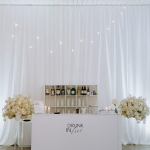 A stylish cocktail bar adorned with elegant white flowers, set against a backdrop of flowing white drapes.