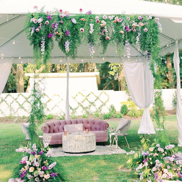 An outdoor lounge beneath a white tent adorned with delightful floral decorations.