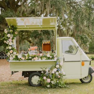 A Piaggio vehicle adorned with vibrant flowers and serving an array of refreshing drinks.